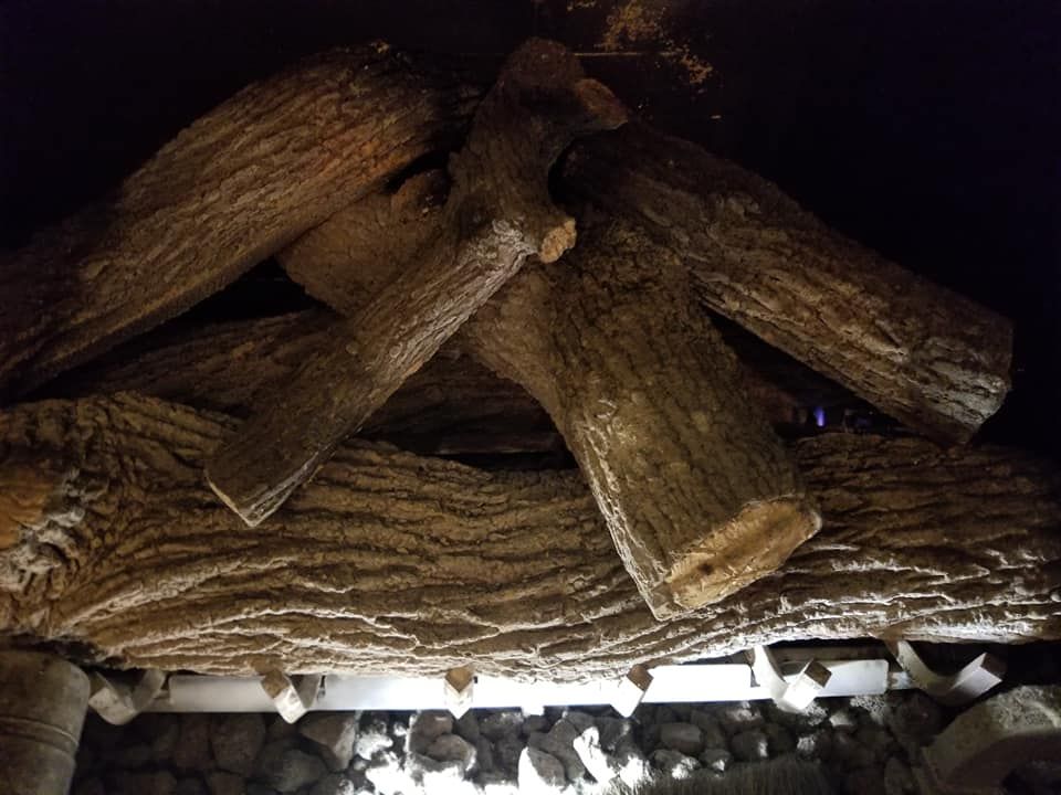 Fireplace with faux wooden logs. Dark setting, logs arranged over a stone hearth.
