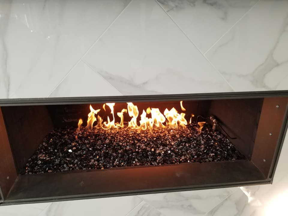 A modern fireplace with flames burning above dark glass rocks, set against white tile.