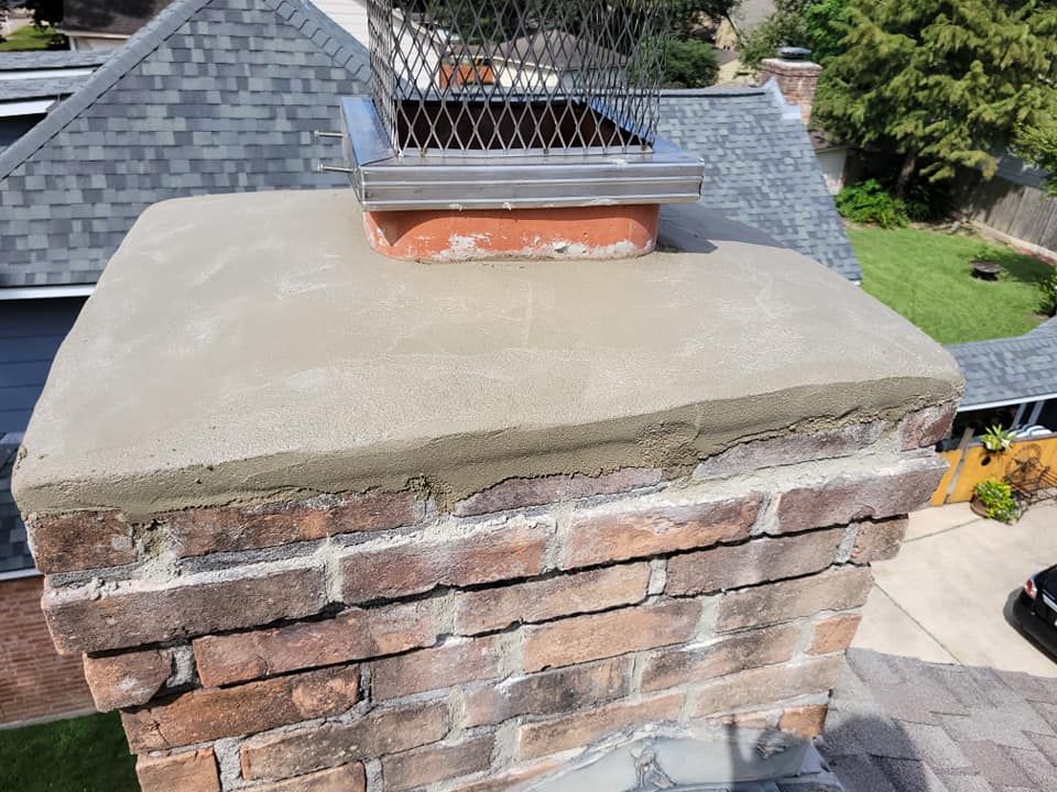 Brick chimney with a concrete cap and a wire mesh chimney cap on a shingle roof.