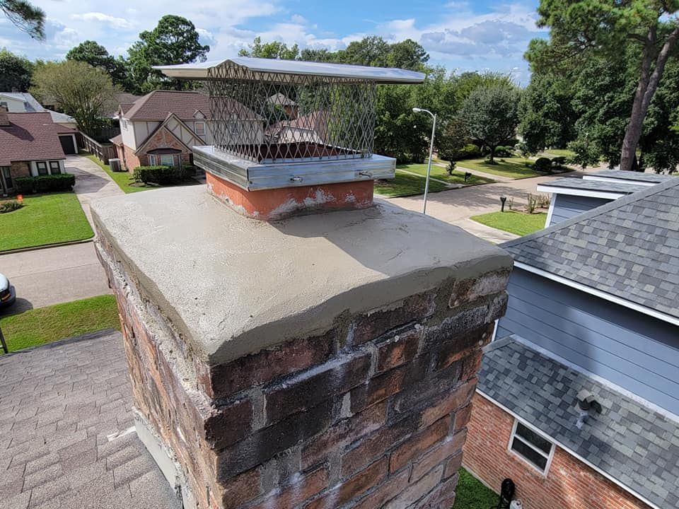 Brick chimney with new concrete cap and metal chimney cap on a sunny day.