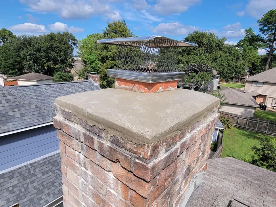 Brick chimney with a new concrete crown and a chimney cap, viewed from a roof on a sunny day.