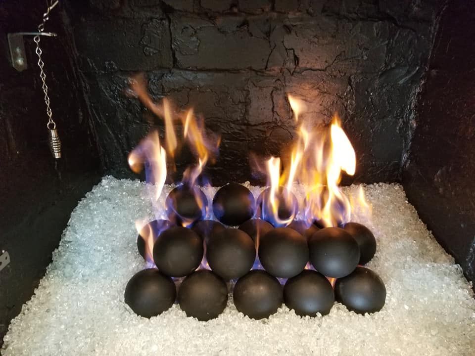 Fireplace with black spheres burning among clear glass stones; flames rise.