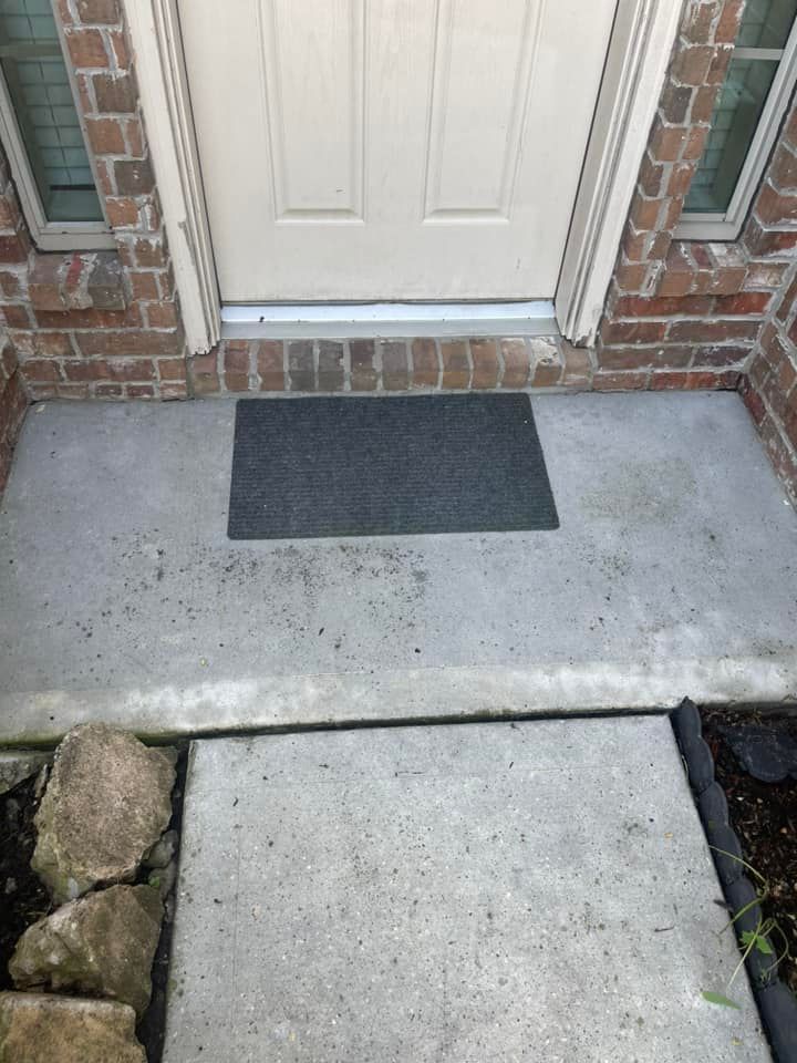 Concrete porch and walkway leading to a beige door, dark gray doormat. Red brick siding.