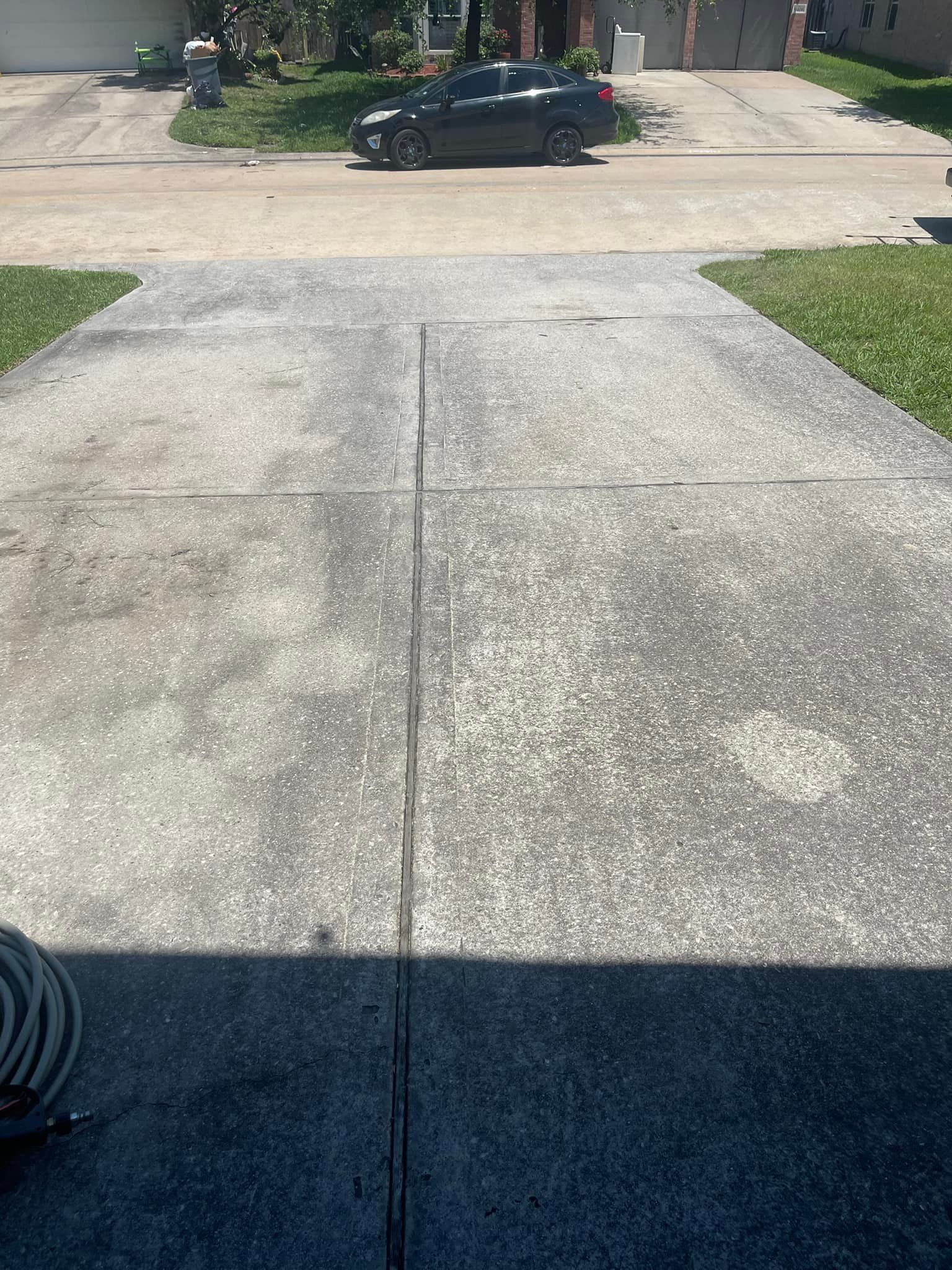 Concrete driveway with cracks, a dark car parked on the street, and grass on either side.