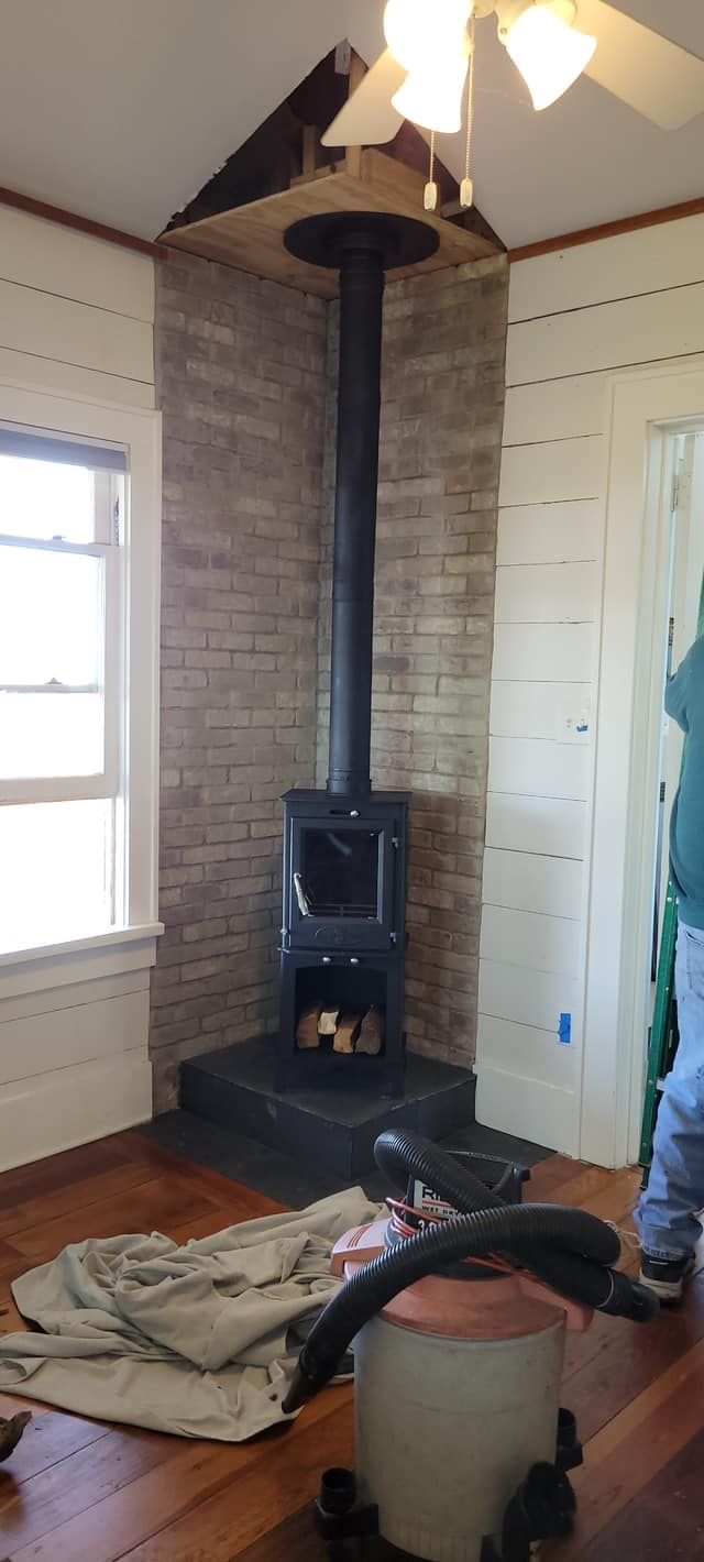 A wood-burning stove installed against a brick wall in a corner. A ceiling fan is overhead.