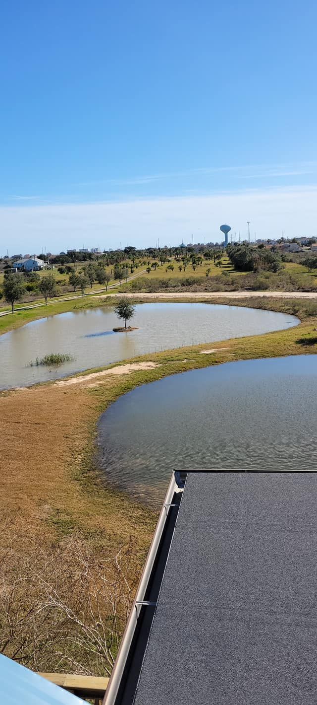View of a pond with a lone tree in the center, and a water tower in the distance under a blue sky.