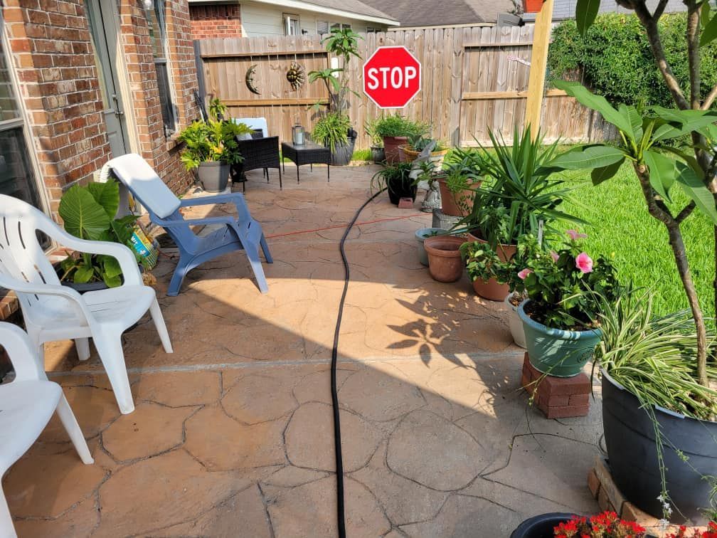 Backyard patio with potted plants, lawn, and chairs. A stop sign is attached to a wooden fence.