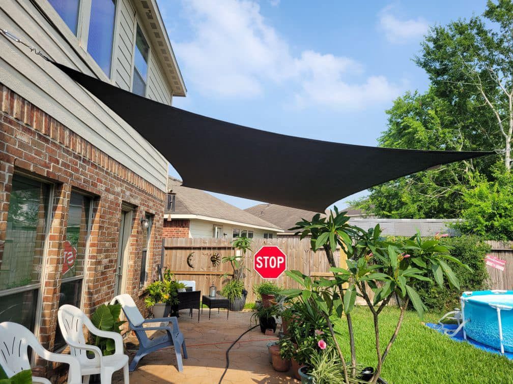 Black shade sail over a patio with chairs and plants. Backyard with a small pool and a stop sign.