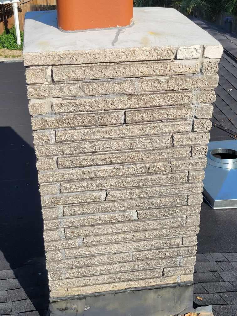 Stone chimney on a rooftop with a brown top.