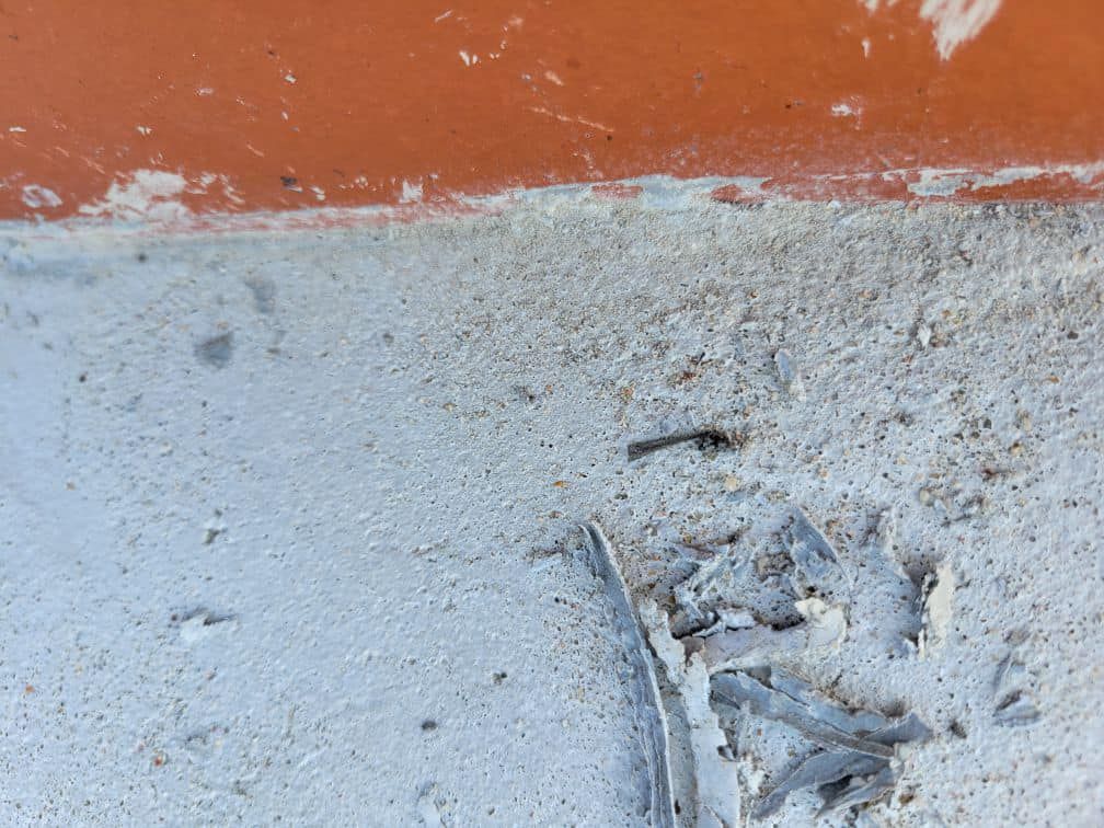 Orange wall meets a light-colored concrete floor with debris.
