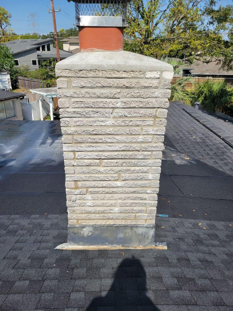 Chimney made of gray brick on a dark shingle roof, with a metal cap.
