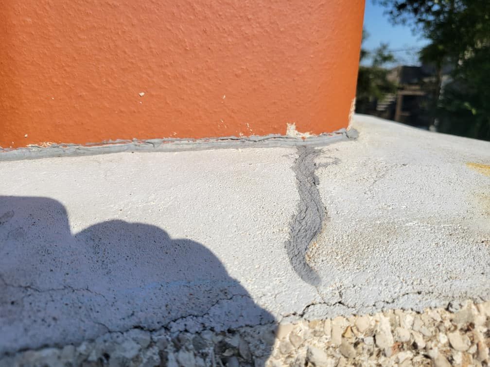 Close-up of a chimney, showing a crack in the concrete base and grey sealant. The chimney is orange.