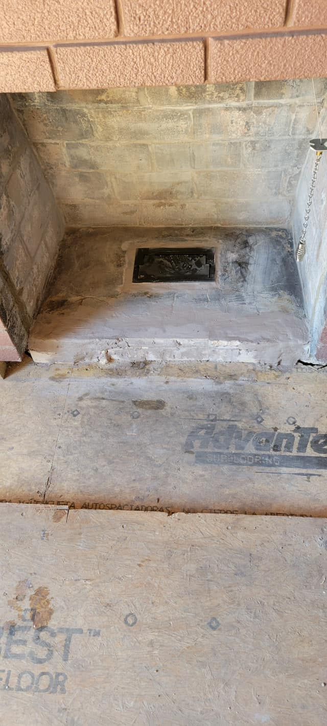 A dirty concrete space, possibly a fireplace, with a vent and brick above.