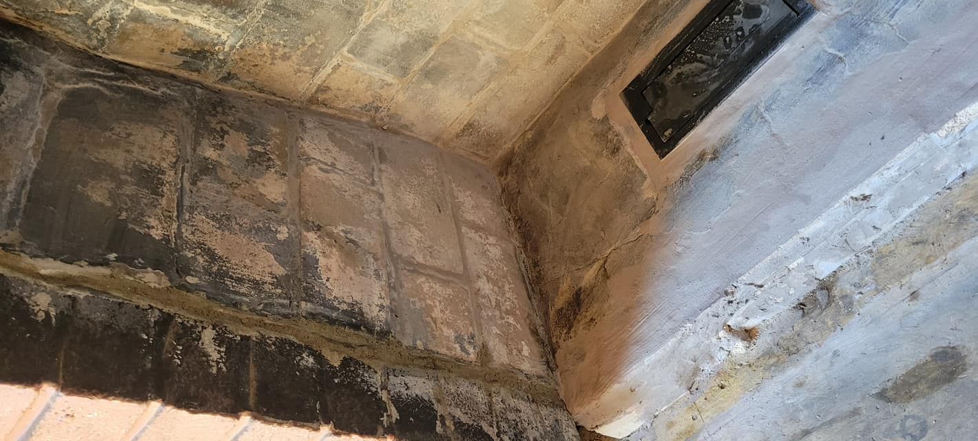 Corner view of aged stone walls and ceiling, with a dark, rectangular inset.