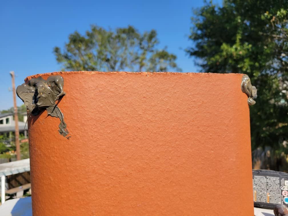 A red cylindrical structure with gray, crumbling material at the top against a blue sky.