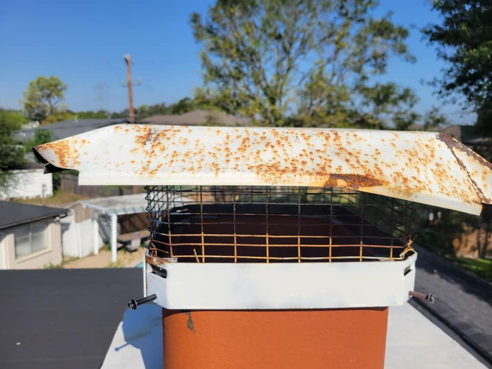 Rusting chimney cap on a brick chimney with a mesh screen, viewed from above, with a blue sky background.