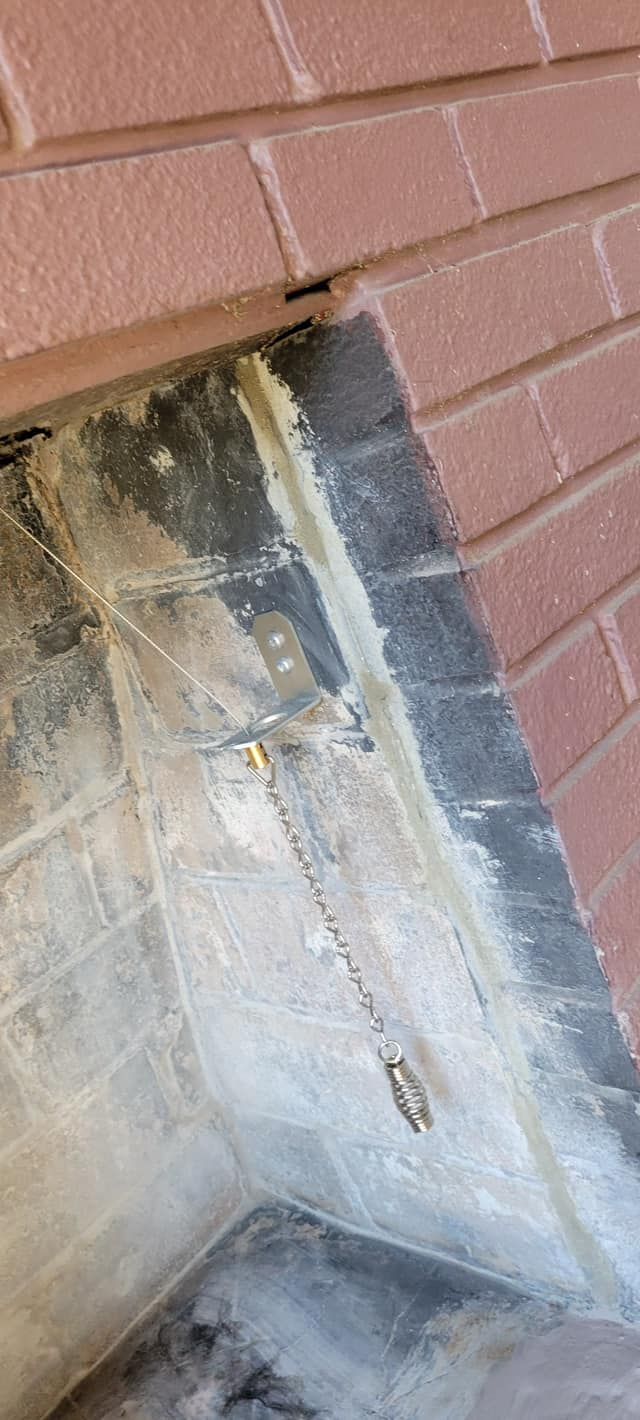 A fireplace interior with brickwork, showing soot and a hanging chain.