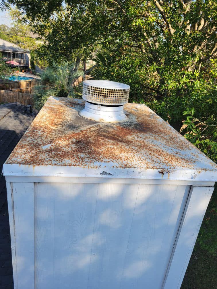 White utility box with rusted top, vent, and surrounding greenery.