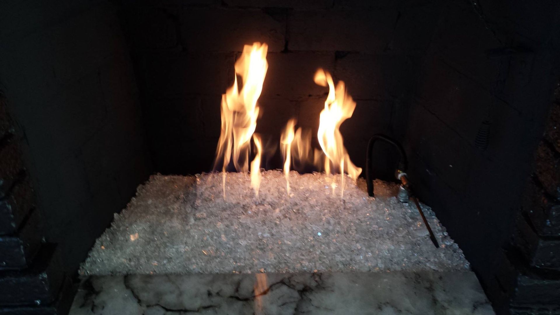 Flames dancing above shimmering, clear glass fire pit, in a dark fireplace.