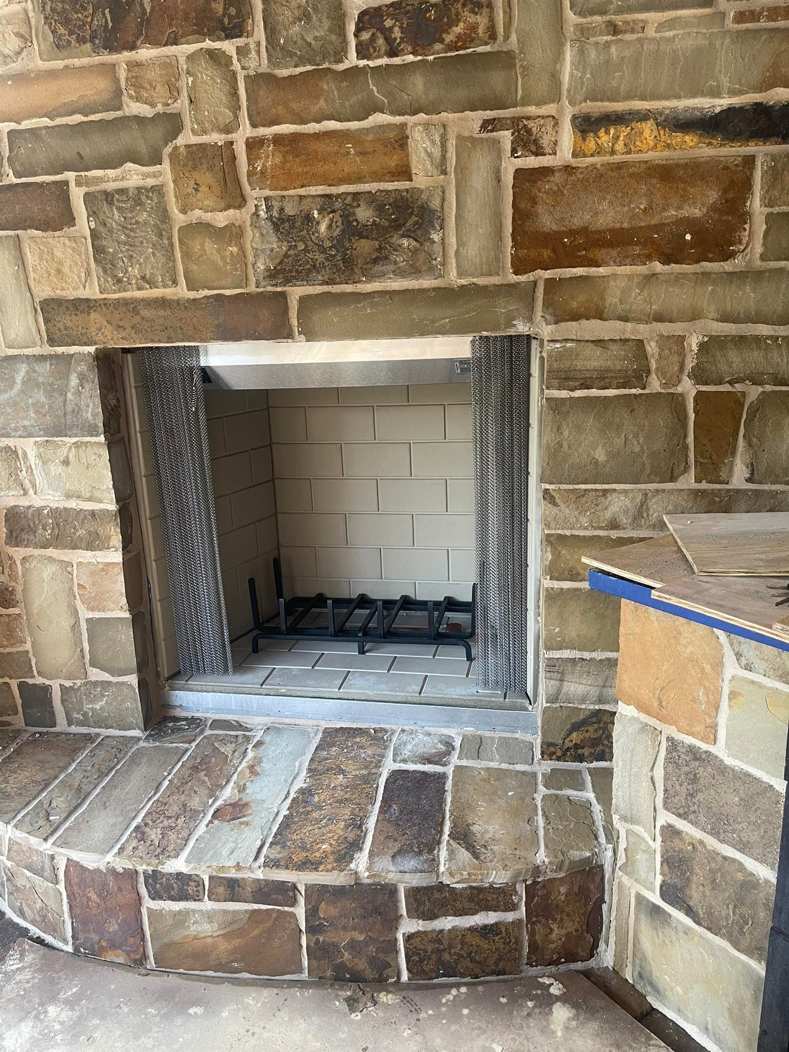 Stone fireplace with rectangular opening and hearth, surrounded by stone.