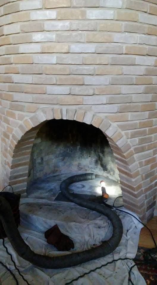 Brick oven with an arched opening, a black hose, and a dirty interior.