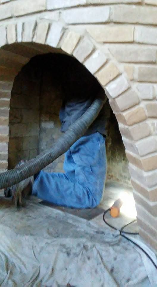Brick arched fireplace interior, blue pants and a gray hose/tube inside, with light and cord visible.