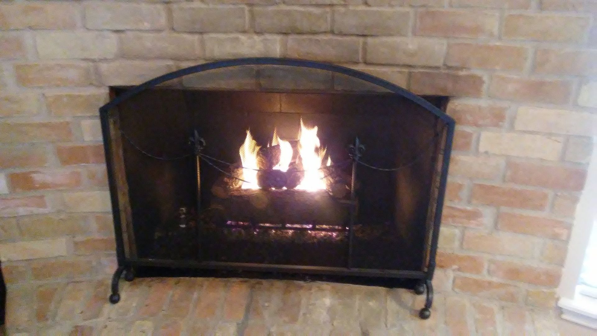 Fireplace with a metal screen and flames against a brick wall.