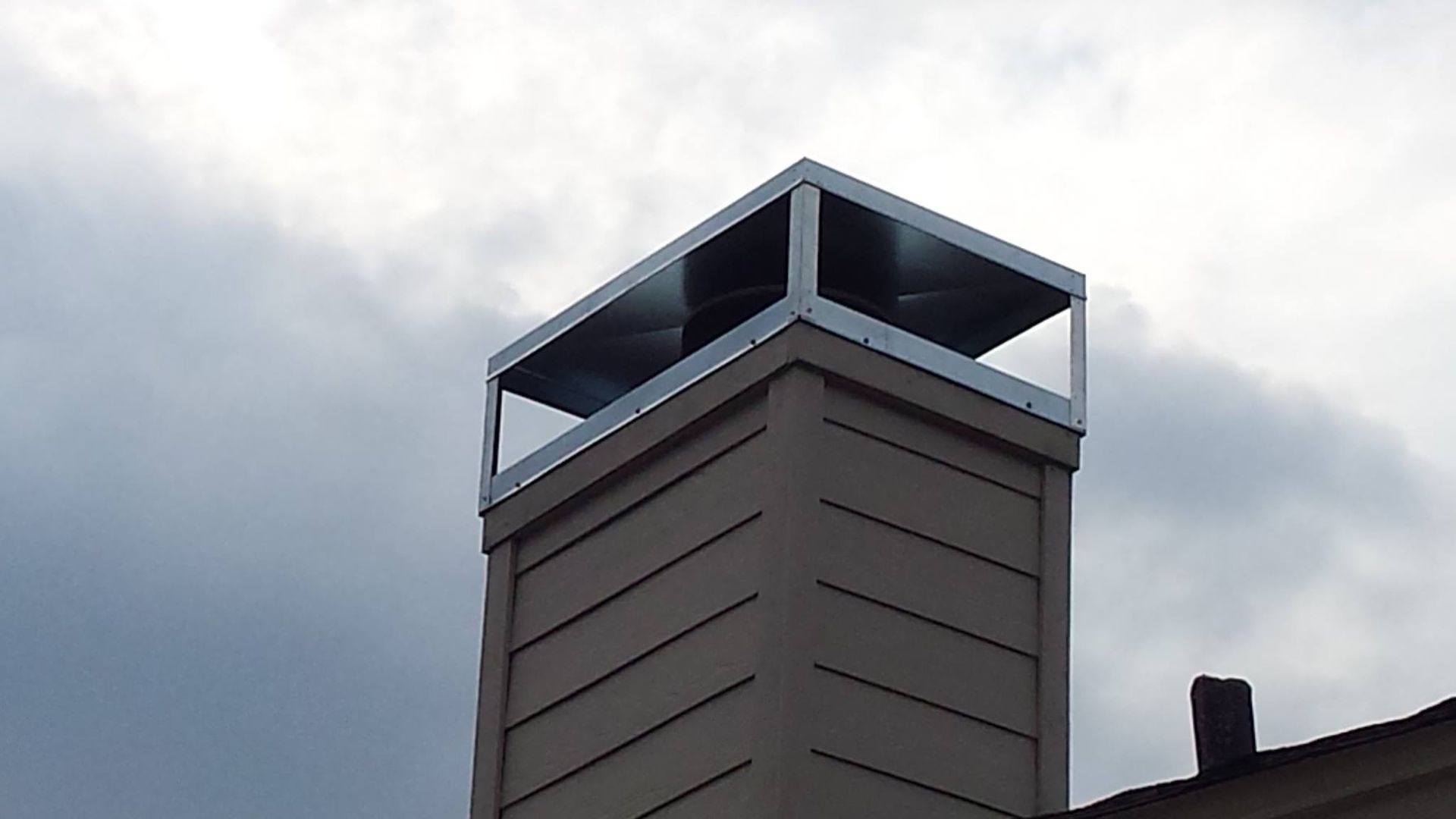 Chimney with a metal cap against a cloudy sky.