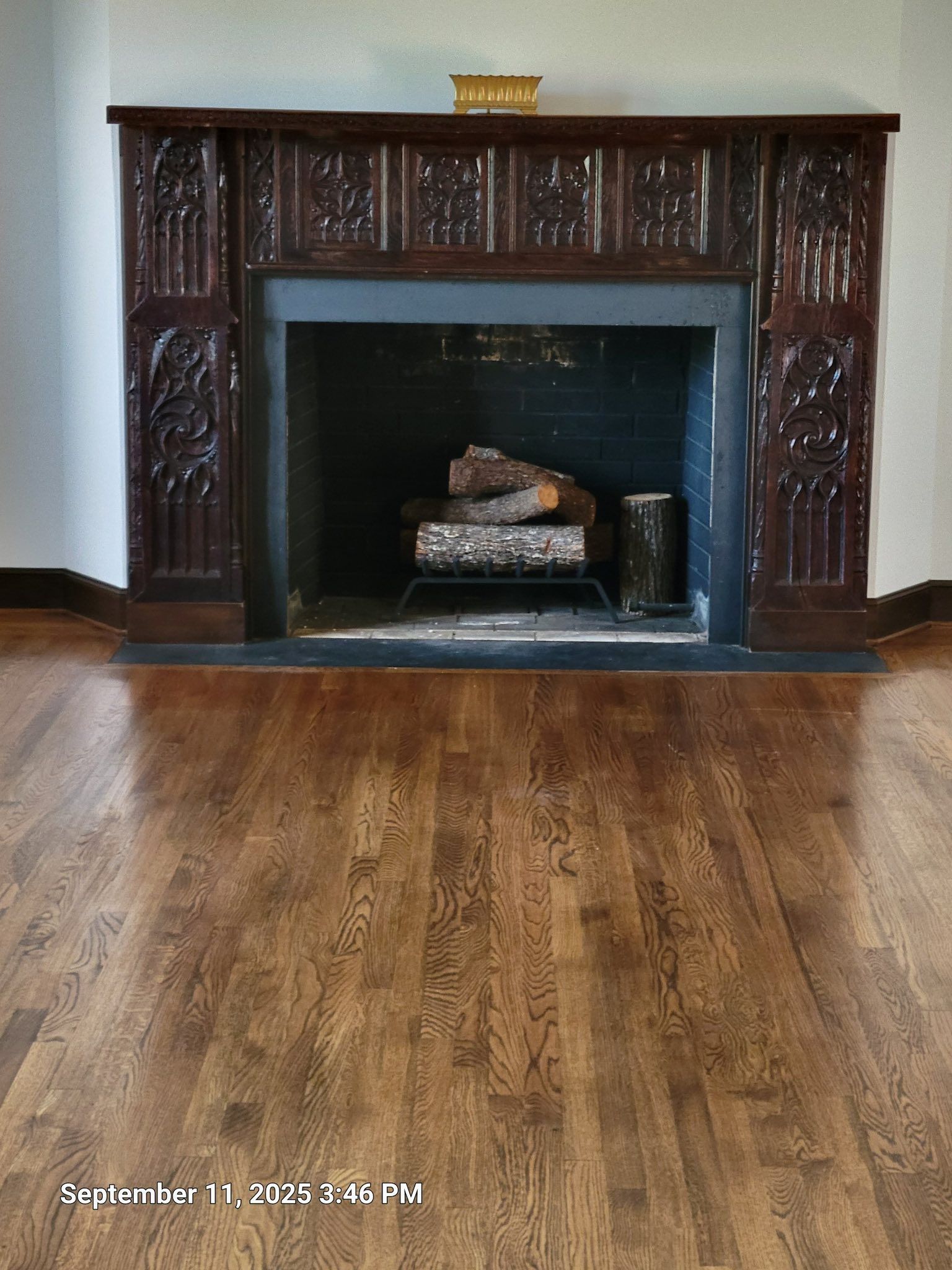 Dark wood fireplace with carved details, set against white wall, hardwood floor.
