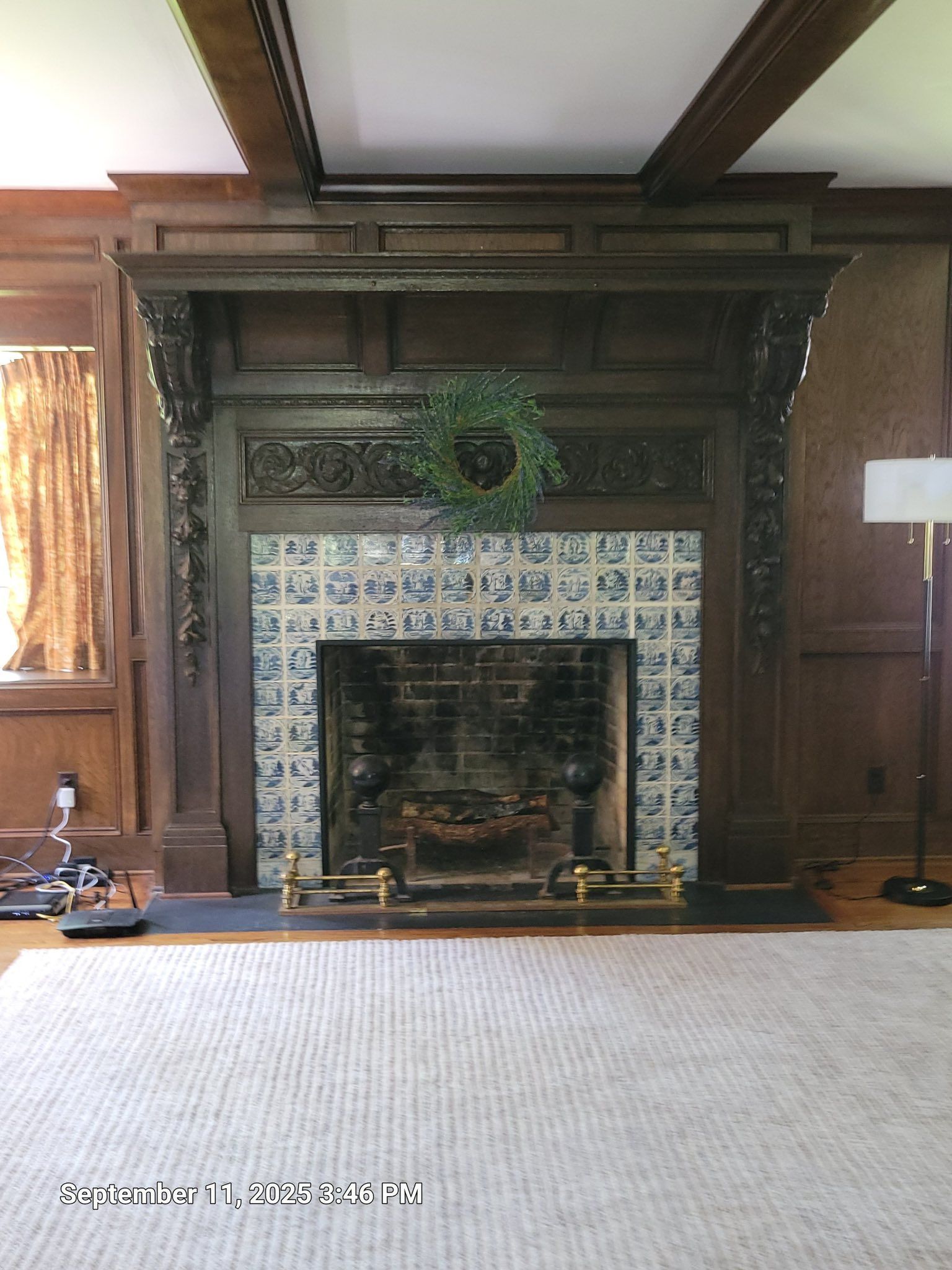Dark wood fireplace with patterned tile surround and a green wreath, in a room with a light carpet.