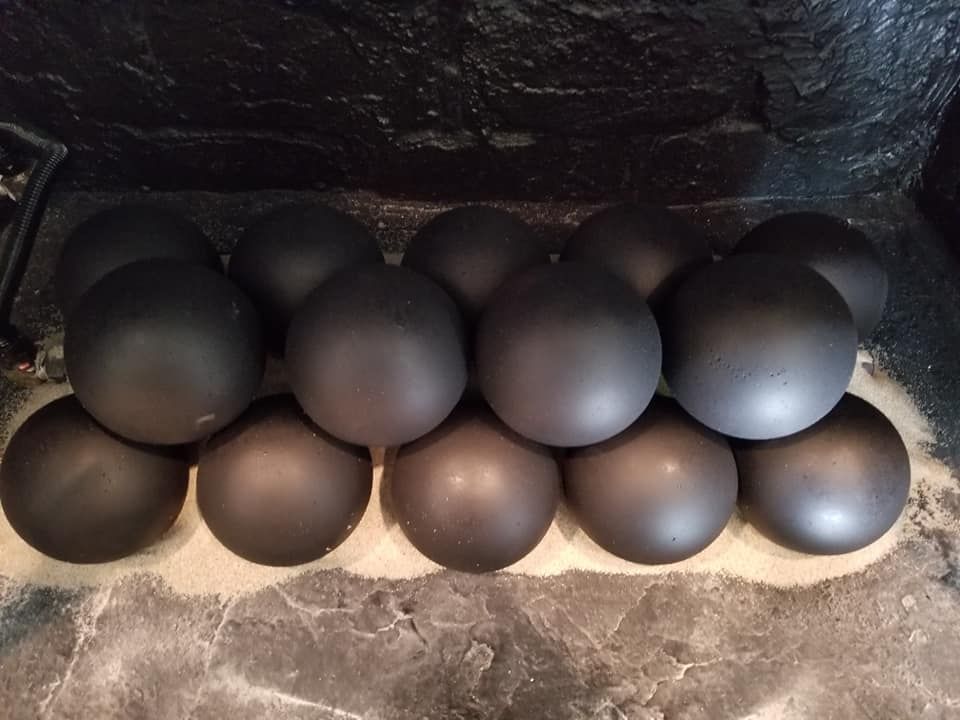 Black cannonballs stacked in a pyramid shape on a stone surface.