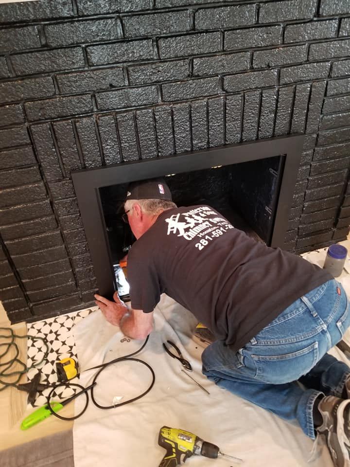 Man installing fireplace insert, kneeling on a cloth. Black painted brick fireplace surround.