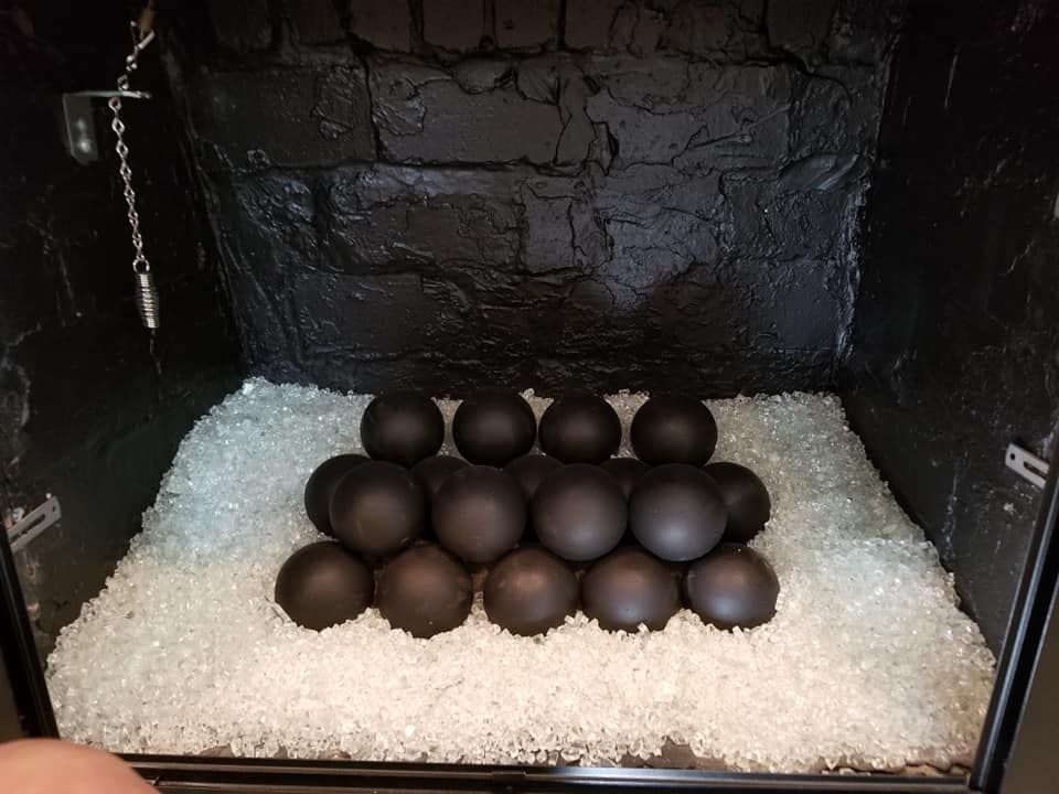 Black fireplace with black spheres nestled on clear glass rocks. Dark brick background.