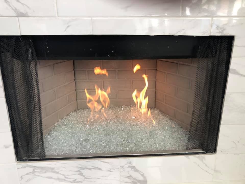 Fireplace with flames rising from clear glass stones, behind a black mesh screen.