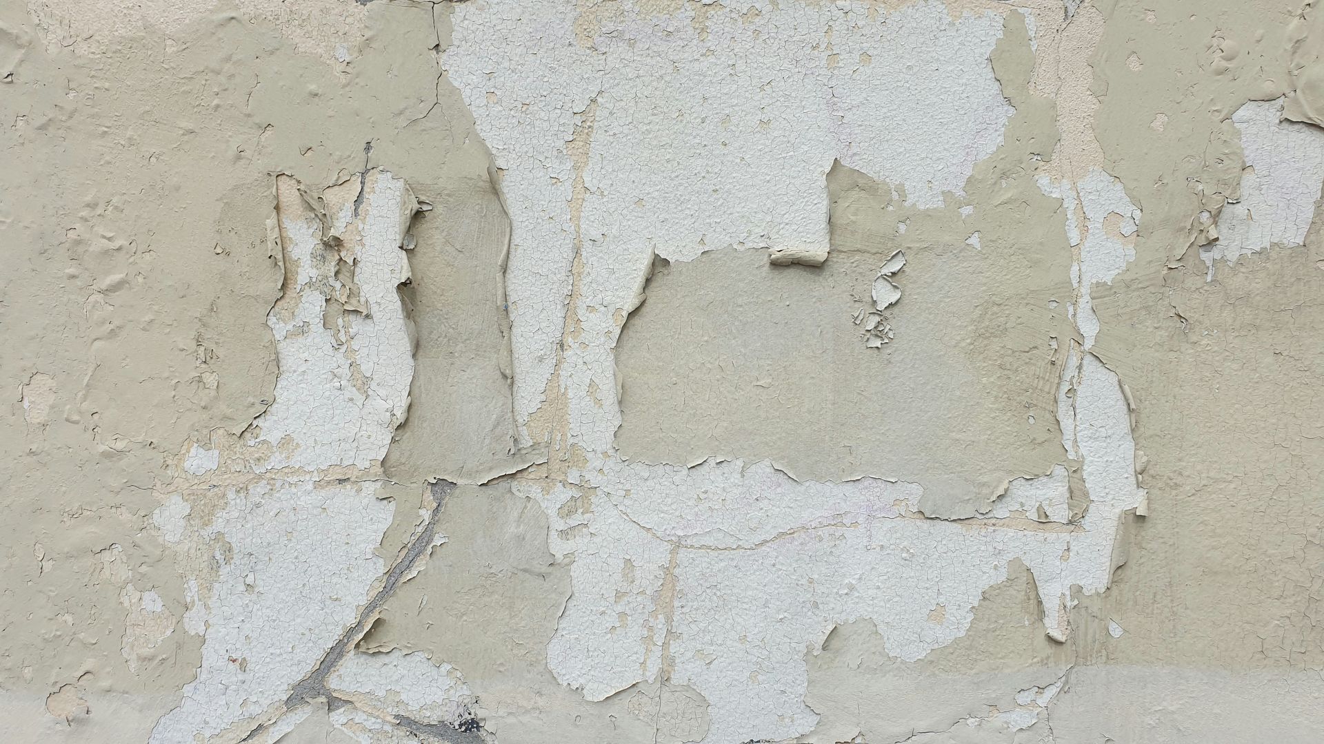 Peeling beige and white paint on a cracked, weathered wall