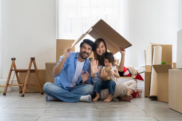 Happy family and toddler girl playing in new home with cardboard boxes.