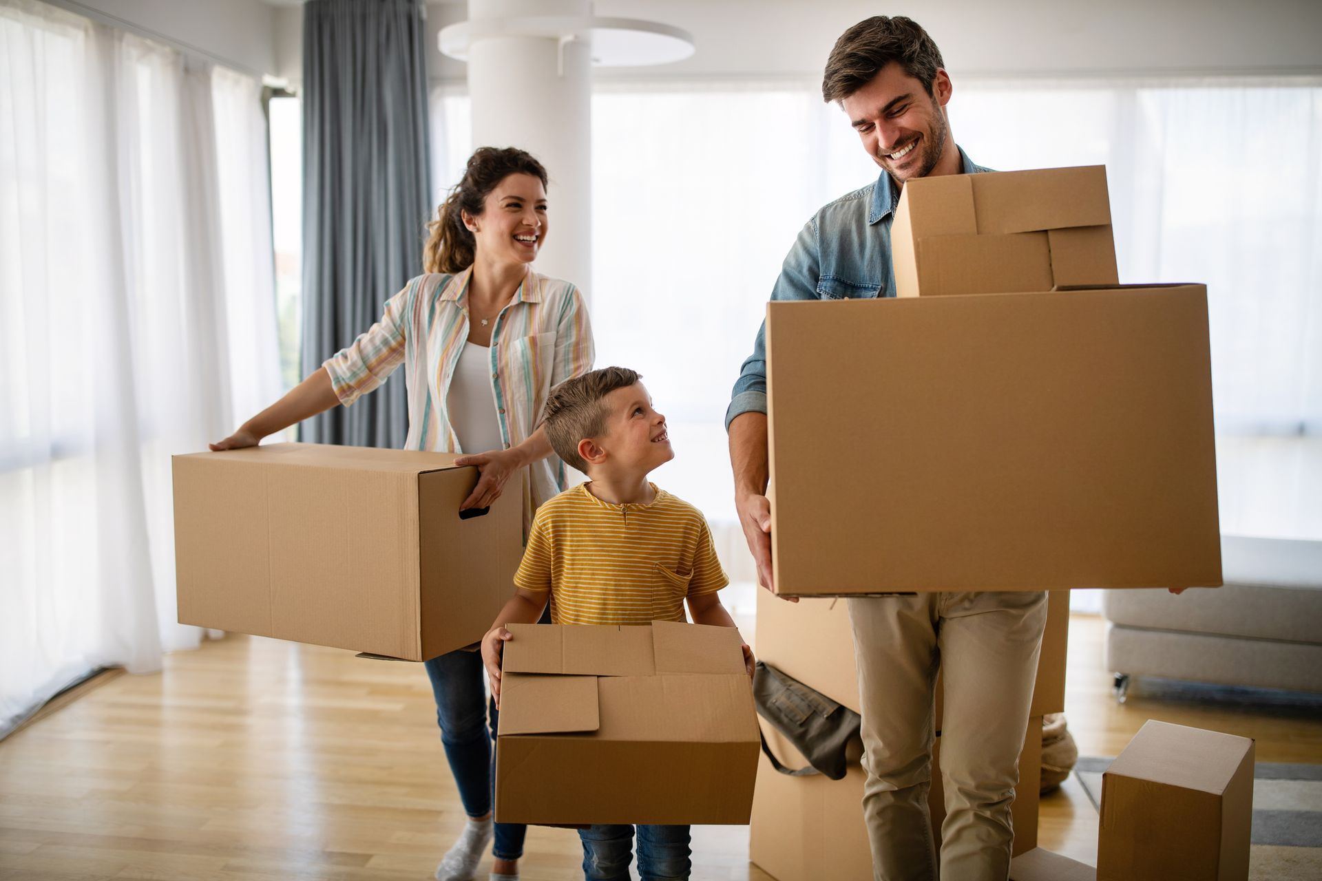Happy young couple with a little boy moving with boxes in a new house.