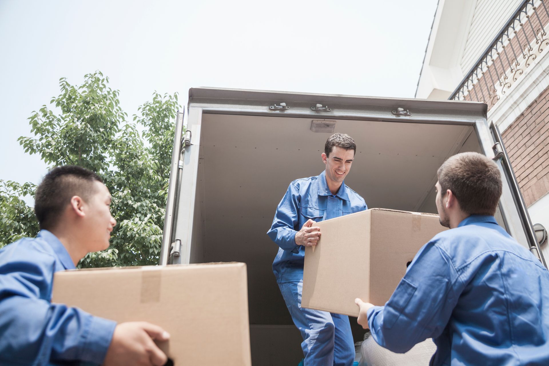 Three movers in blue uniforms from Central Van & Storage carry boxes, showcasing professional moving services.