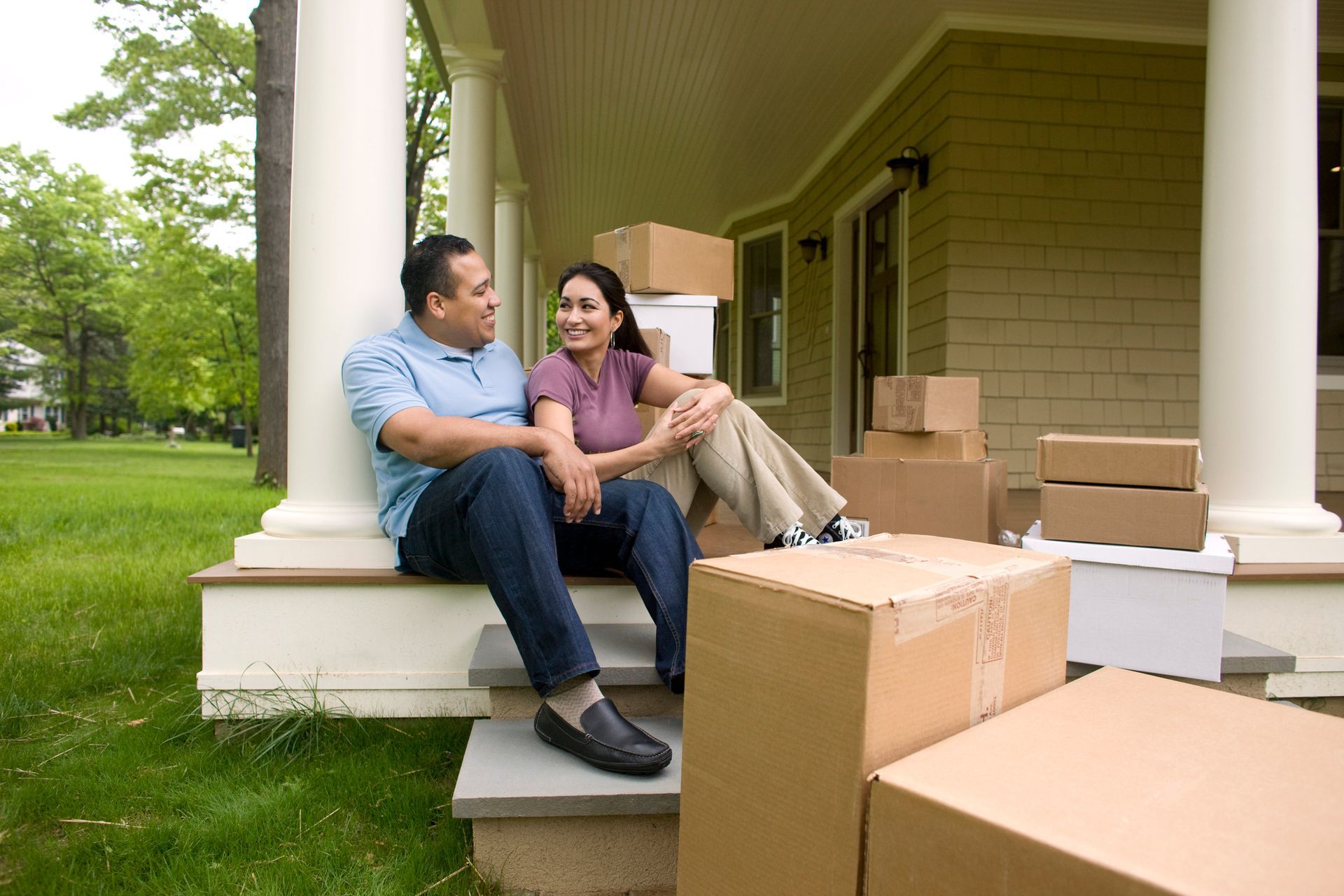 Happy couple with moving boxes, talking on a porch.