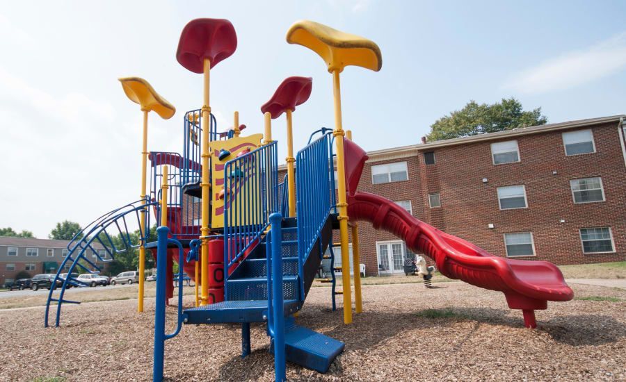 A colorful playground with a red slide in front of a brick building at Westgate Apartments & Townhomes in Manassas, VA.