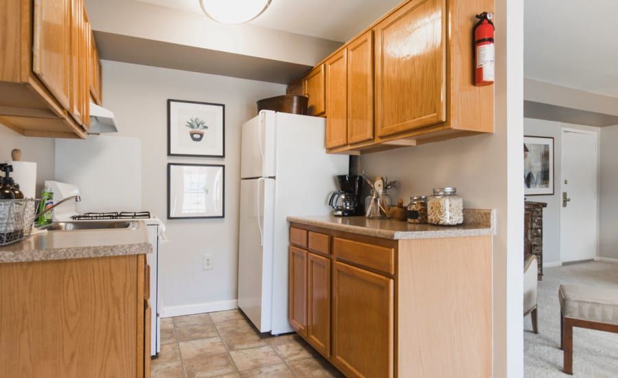 A kitchen with wooden cabinets , a refrigerator , stove , sink and fire extinguisher at Westgate Apartments & Townhomes in Manassas, VA.