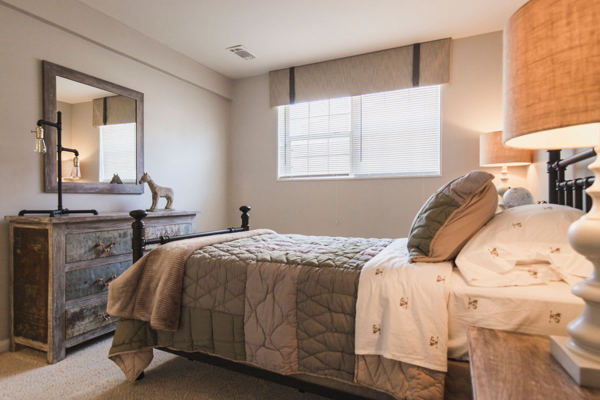 A bedroom with a bed , dresser , lamp , mirror and window at Westgate Apartments & Townhomes in Manassas, VA.