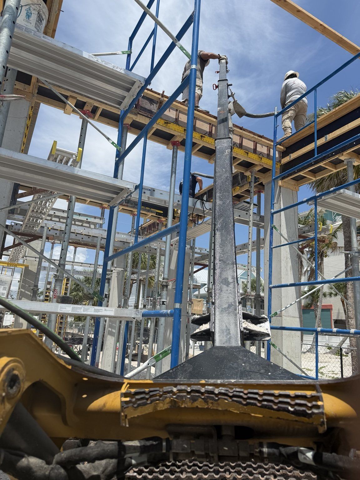 Construction workers on blue scaffolding above a yellow excavator at a building site