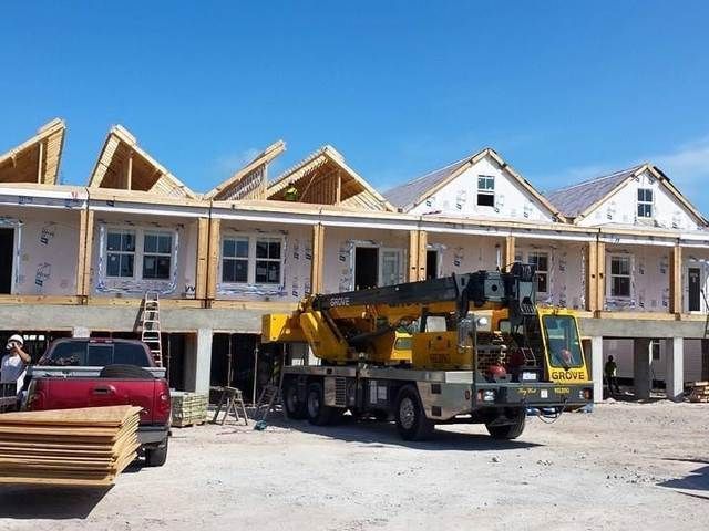 Construction site with row houses under construction, a crane truck, and stacked lumber under a blue sky.