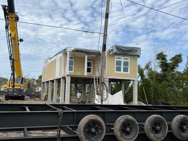 Yellow house being lifted by a crane onto a flatbed trailer at a construction site.