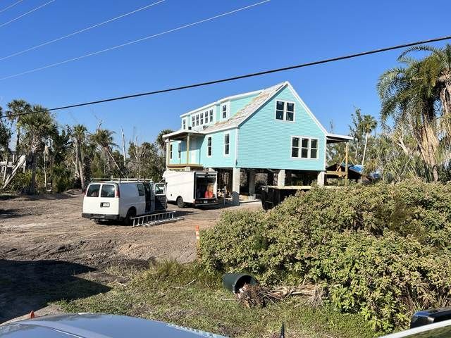 Turquoise stilt house with white vans parked beside it under a clear blue sky.