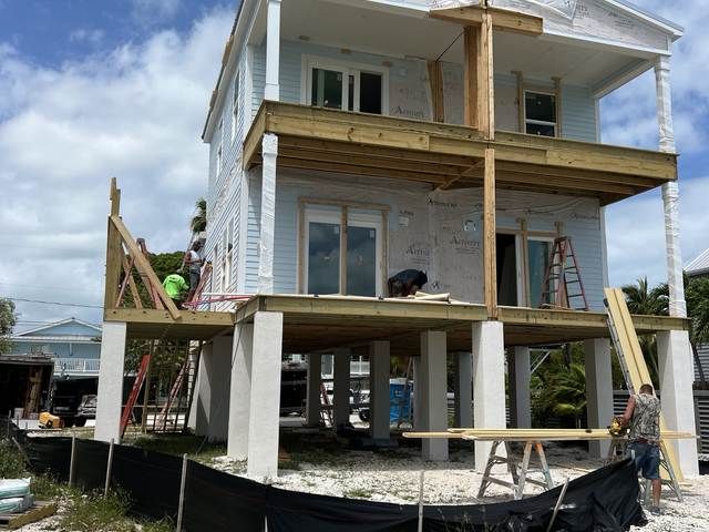 House under construction with workers on scaffolding and lumber framing around a white two-story exterior.