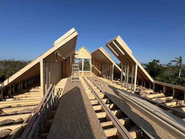 Wood-framed house under construction with exposed rafters and a blue sky overhead.