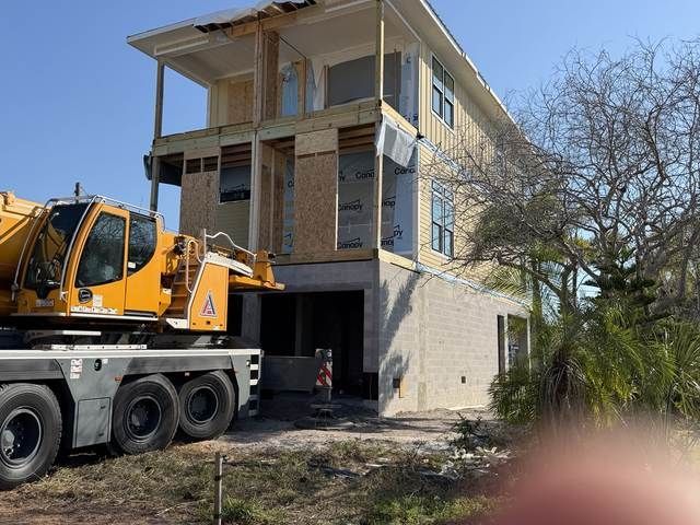 Yellow construction crane beside a two-story house under renovation, with open ground-floor garage.