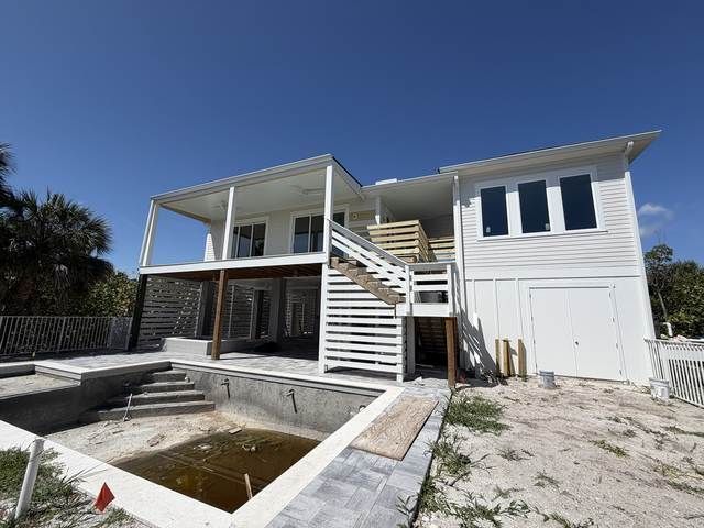 White two-story house with wraparound porch, exterior stairs, and a partially filled rectangular concrete pool in front.